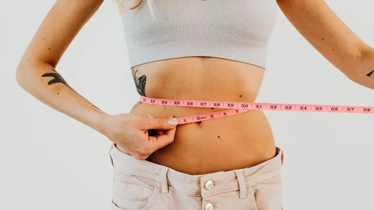 Kobieta mierzy talię centymetrem. Efekty diety 1400 kcal są widoczne.