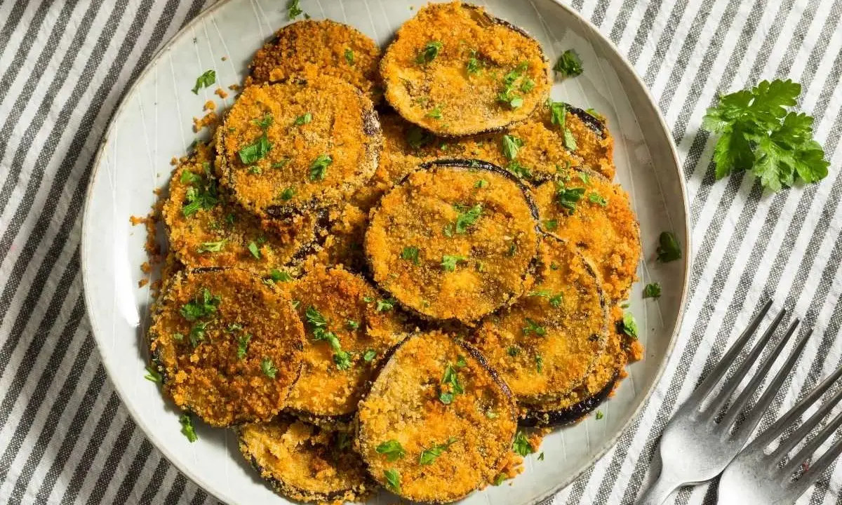 Plato de berenjenas rebozadas, doradas y crujientes, espolvoreadas con perejil fresco.