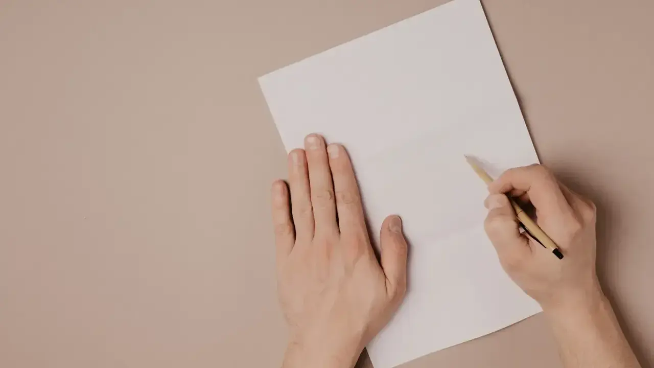 Ręce piszą list motywacyjny po angielsku na białej kartce.