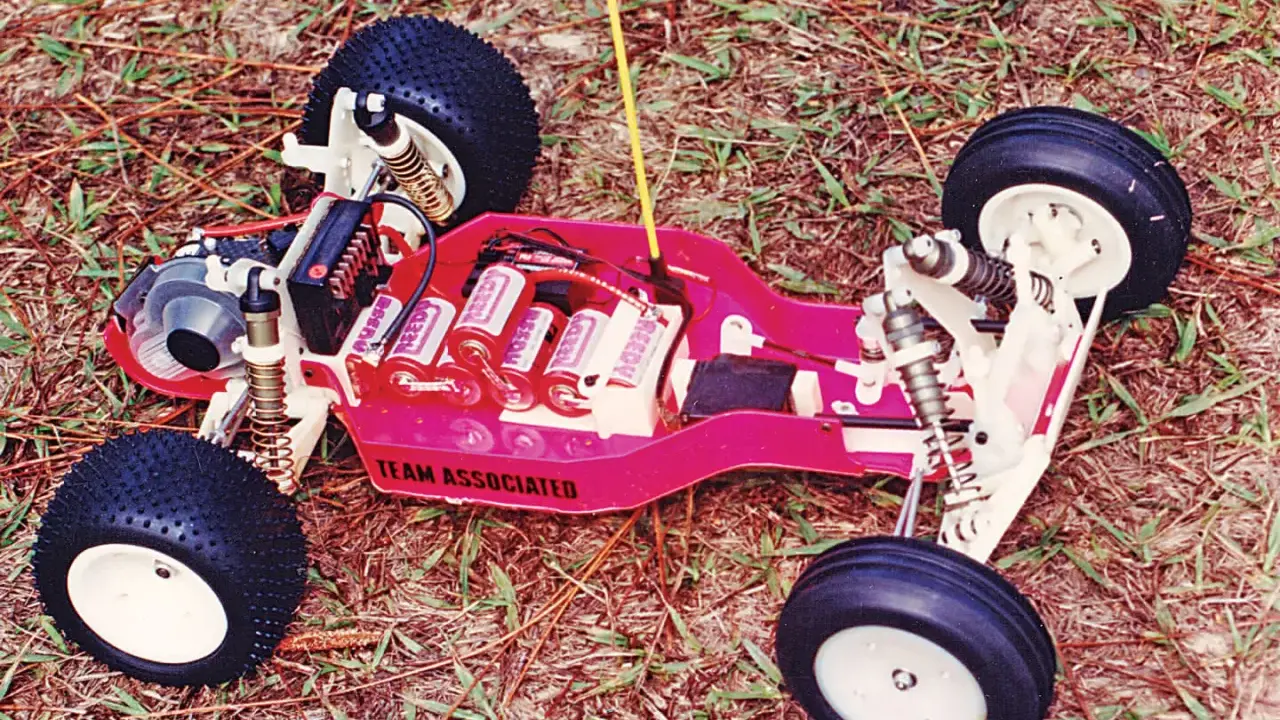 Ein ferngesteuertes Auto von Team Associated mit Batterien und Reifen auf Gras.