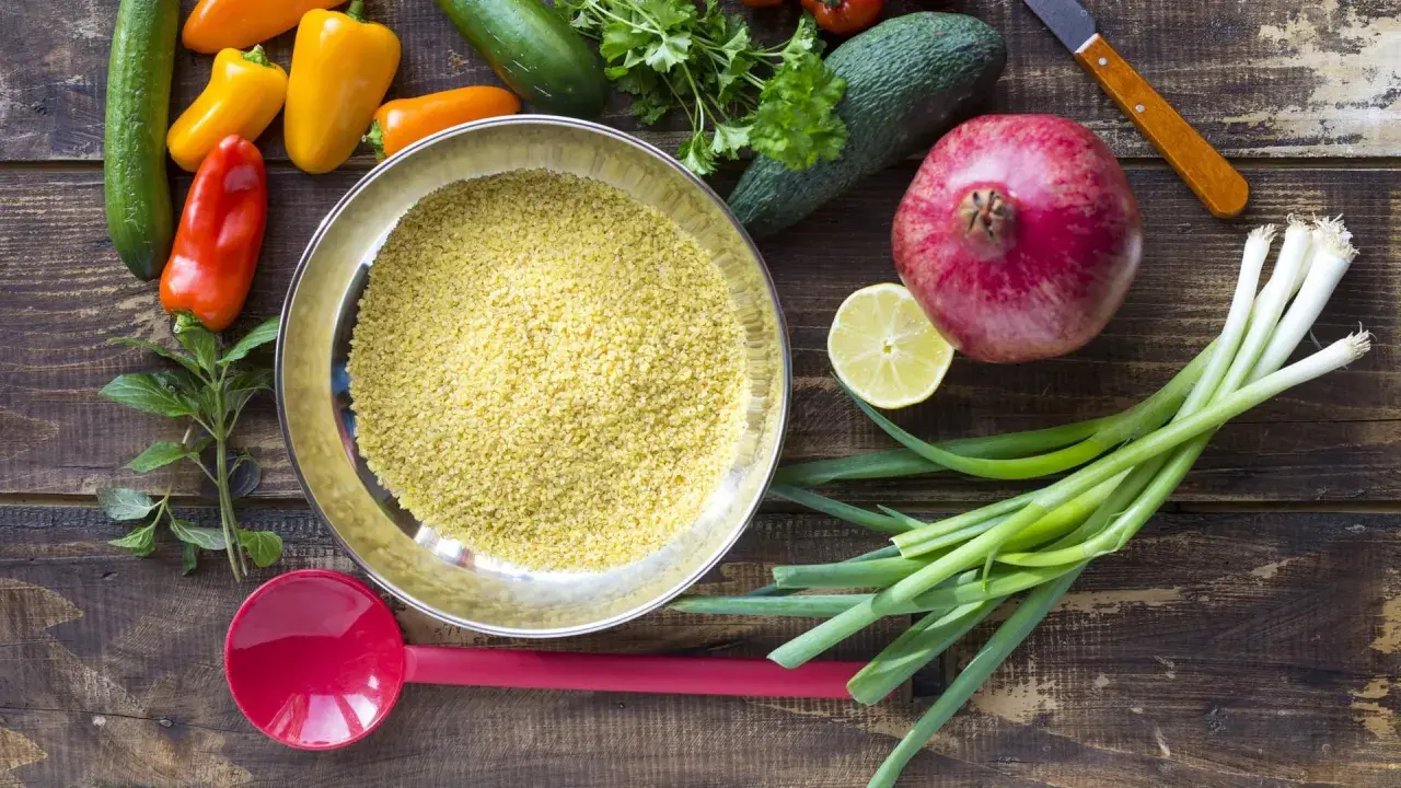 Schüssel mit Bulgur, einer tollen Quelle für **bulgur protein**, umgeben von frischem Gemüse wie Paprika, Gurken, Granatapfel und Frühlingszwiebeln.