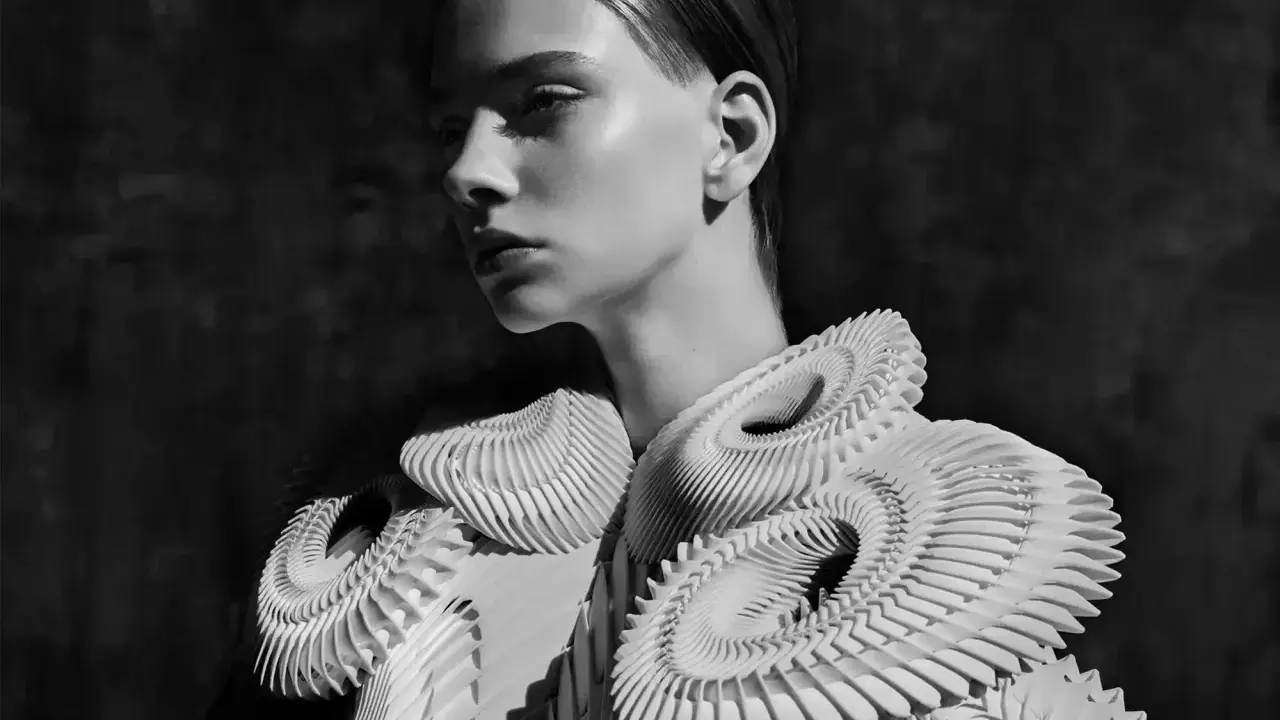 A model showcases intricate, sculptural white garments, embodying futuristic fashion. The avant-garde design features layered, organic shapes that create a dramatic silhouette.
