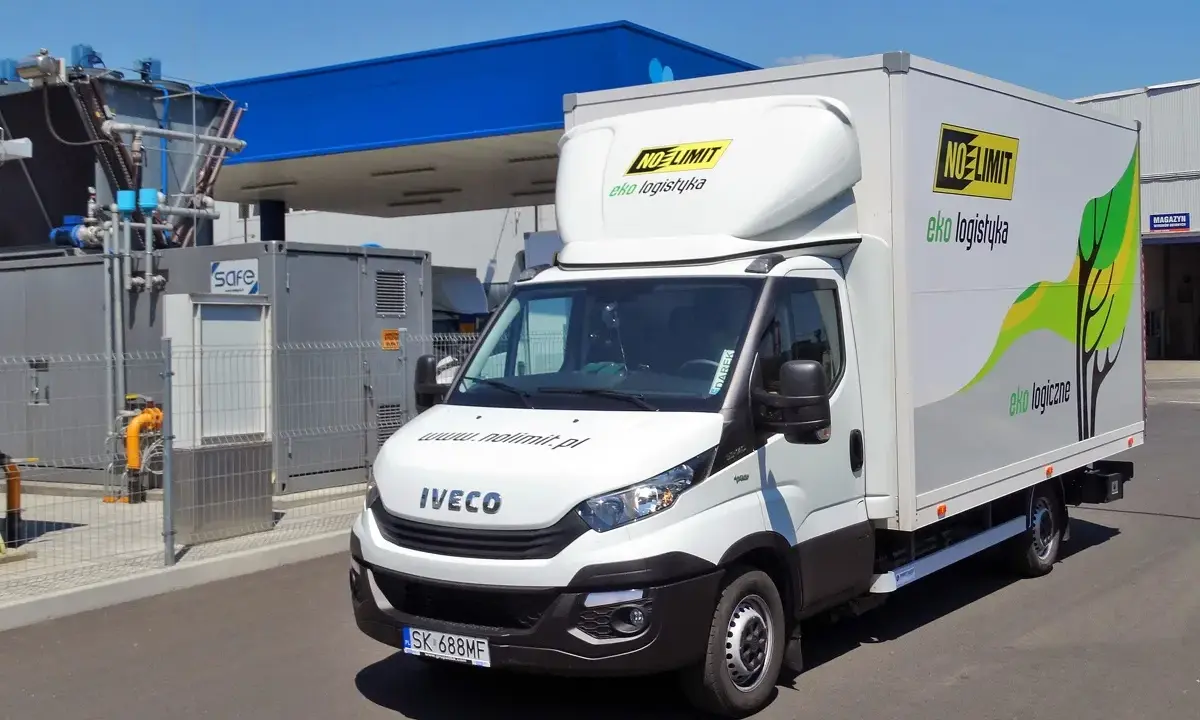 Biała ciężarówka Iveco zasilana gazem CNG, z logo "NO LIMIT eko logistyka", zaparkowana przy stacji paliw.