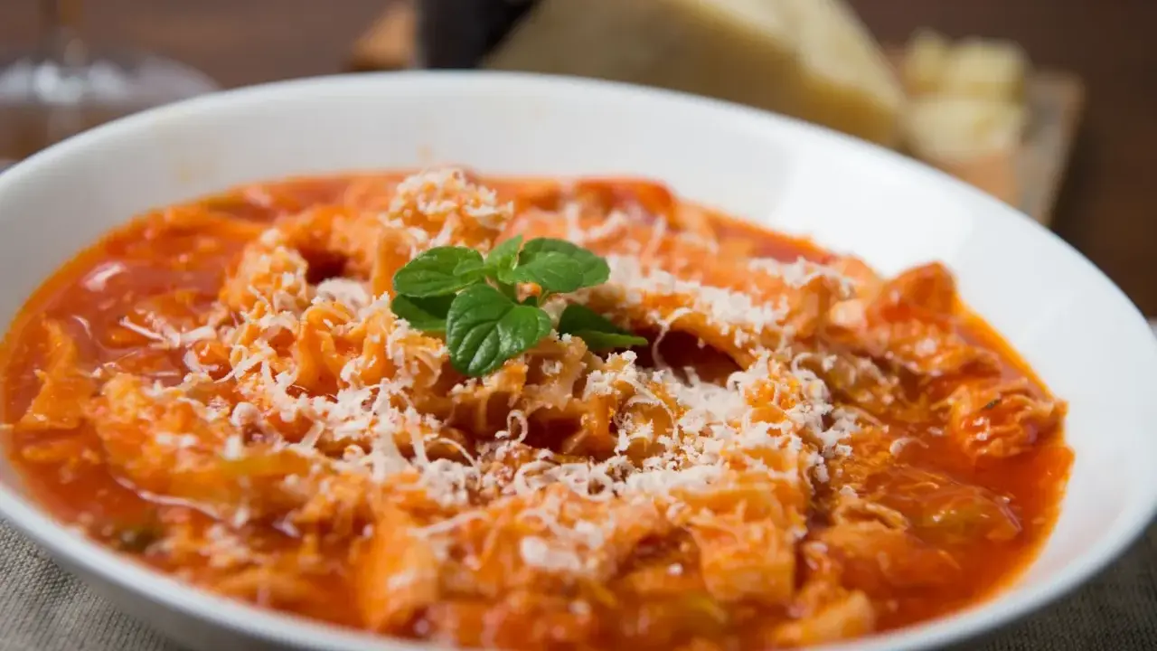 Trippa alla romana, uno dei piatti tipici del Lazio, servita in una ciotola bianca con parmigiano grattugiato e una fogliolina di menta.