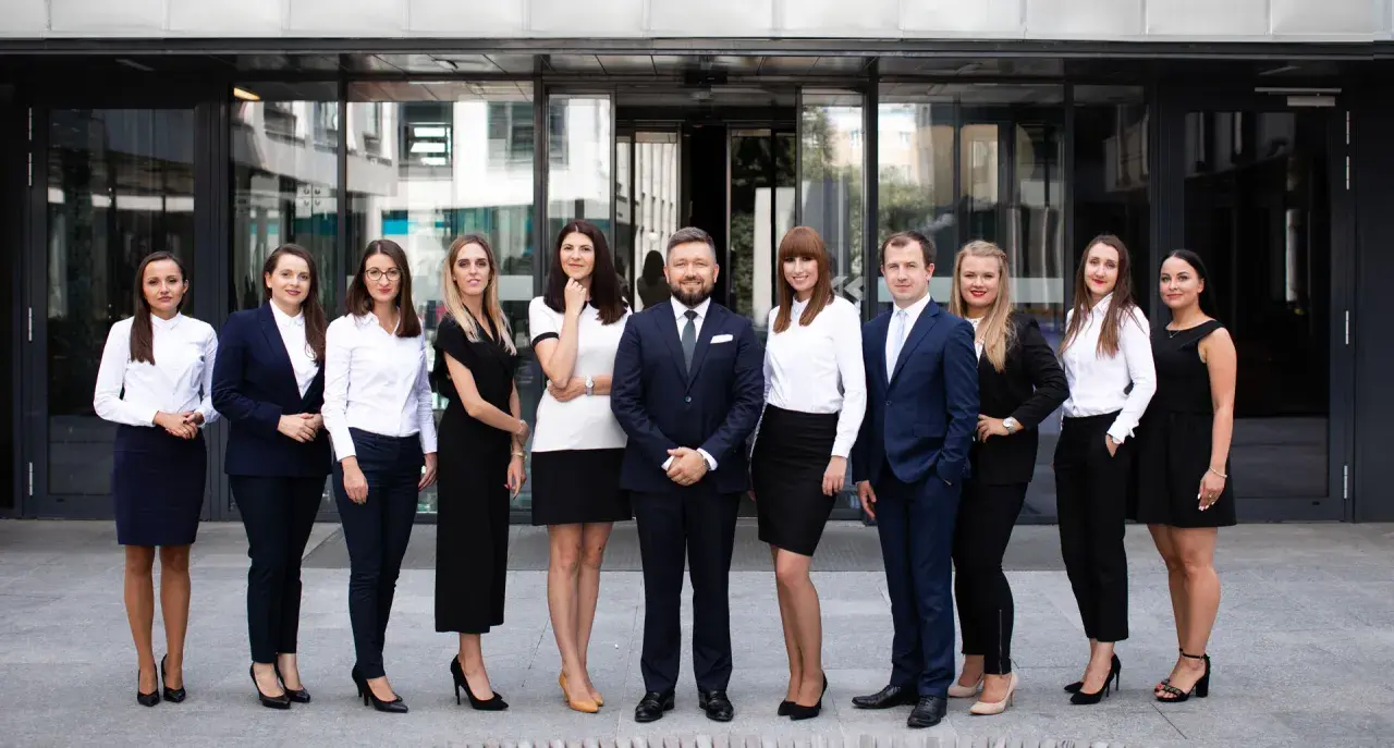 Grupa profesjonalistów w eleganckich strojach stoi przed nowoczesnym budynkiem.