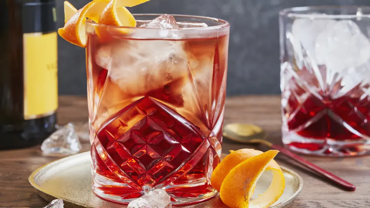 Ein erfrischender Negroni Sbagliato mit Eis und Orangenzeste, serviert auf einem goldenen Teller.