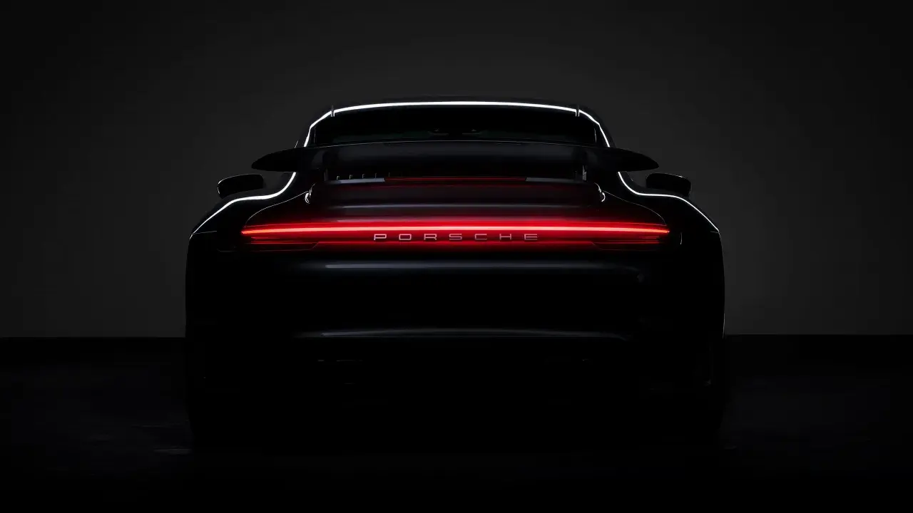 Ein schwarzer Porsche von hinten, dessen Rückleuchten in einem leuchtenden Rot erstrahlen und den Schriftzug "PORSCHE" beleuchten.
