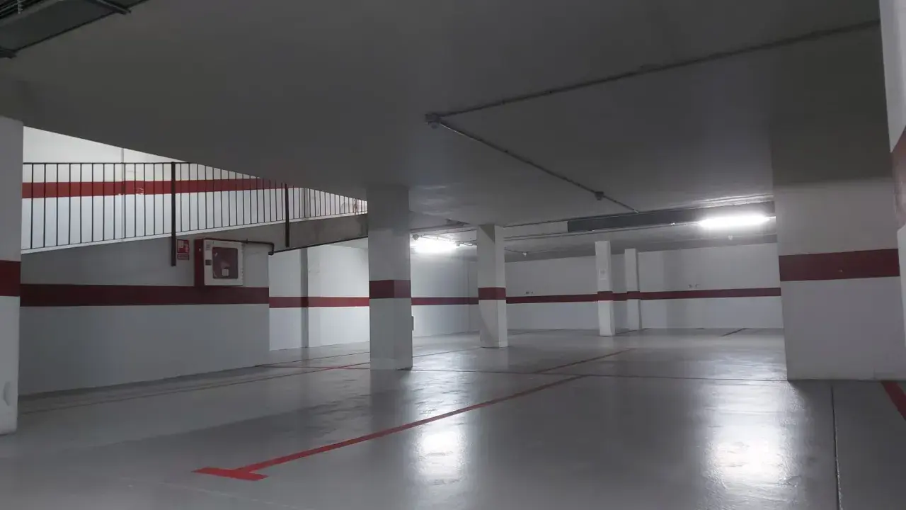 Suelo de garaje recién pintado, con líneas rojas y grises que marcan las plazas.