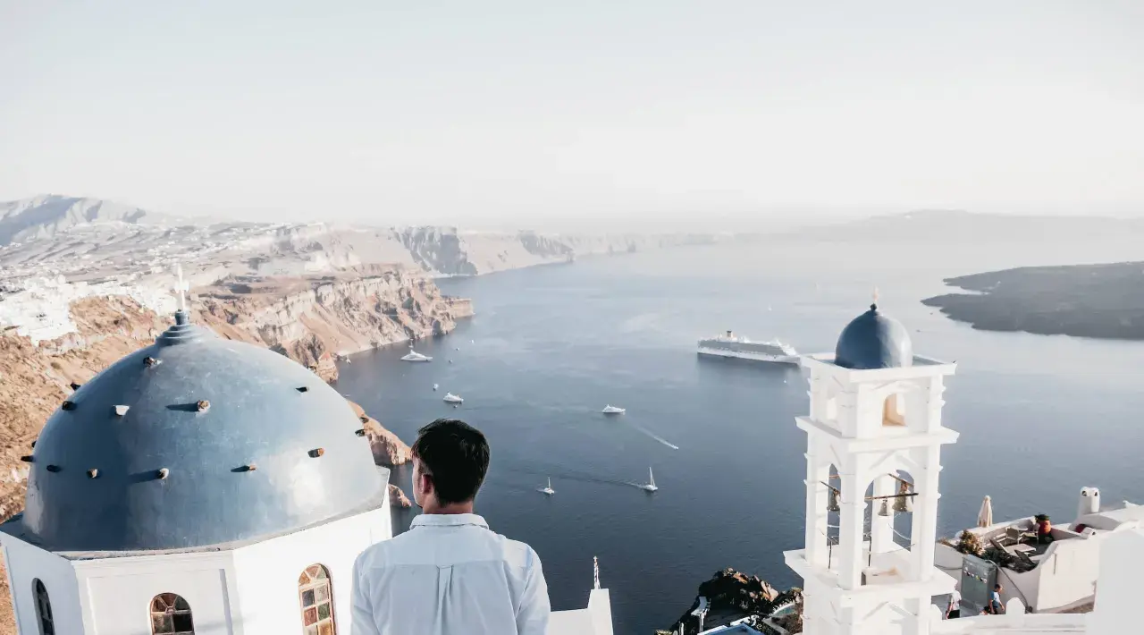 A man gazes at the caldera on a gay Greek island, with iconic blue domes and white architecture overlooking the Aegean Sea.