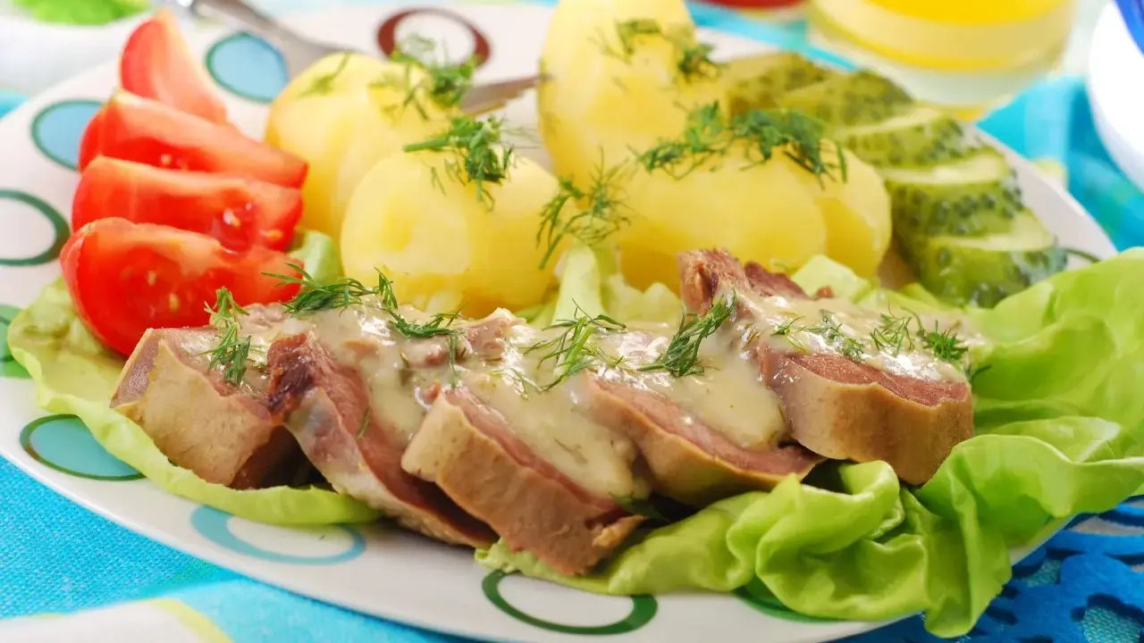 Kawałki ozorków w sosie chrzanowym, podane z ziemniakami, pomidorami i ogórkiem kiszonym. Danie ozdobione jest świeżym koperkiem.