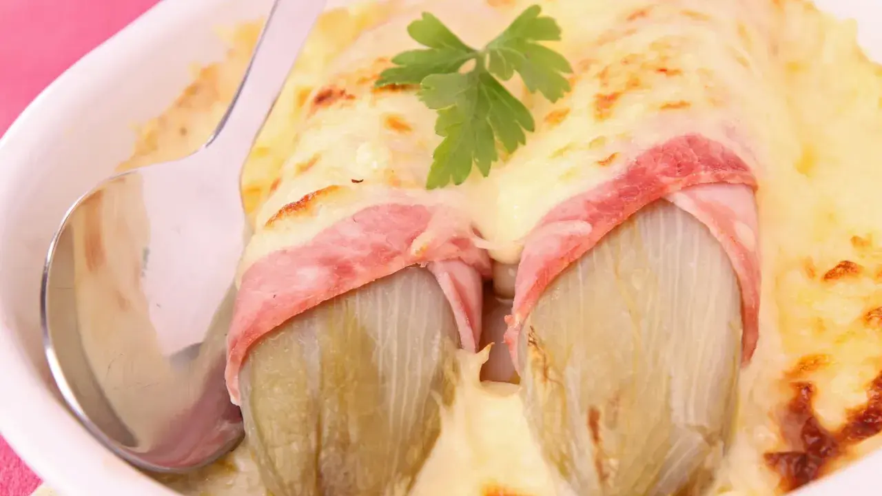 Deux endives braisées enveloppées de jambon, nappées de fromage fondu et gratiné, garnies d'une feuille de persil. Un plat réconfortant.