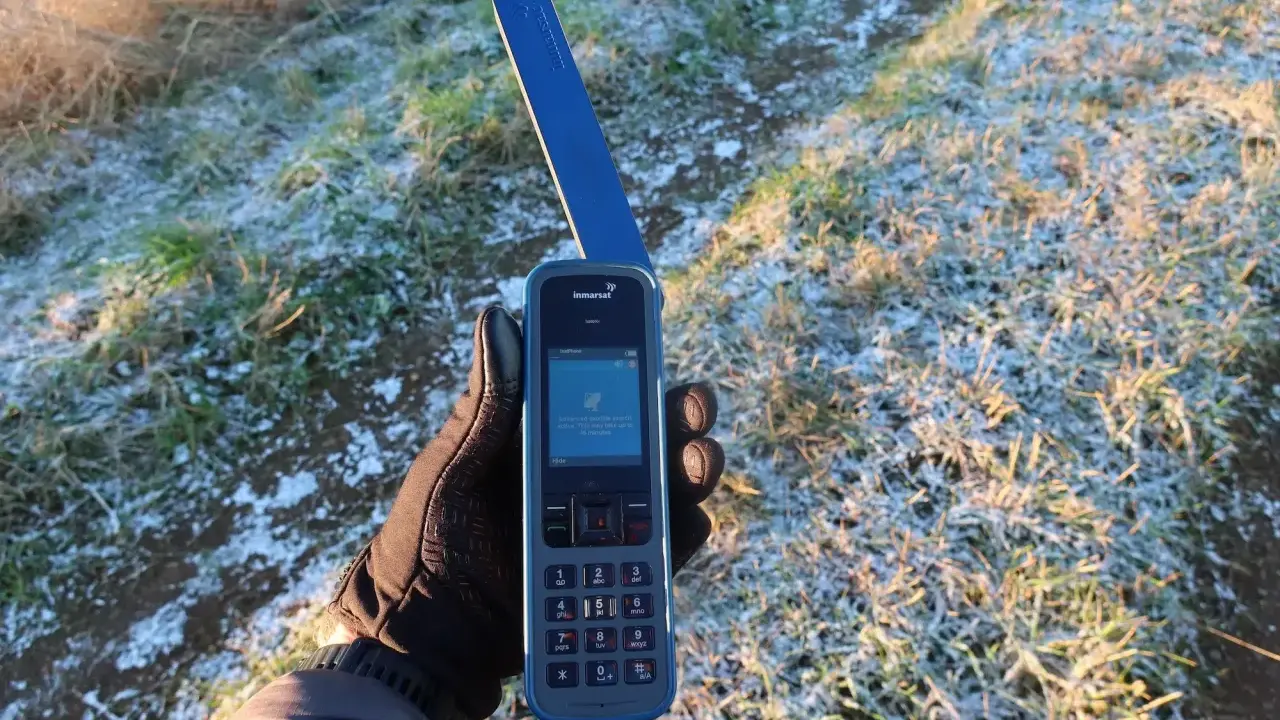 Ręka w rękawiczce trzyma telefon Inmarsat IsatPhone, gotowy do nawiązania połączenia przez telefonię satelitarną w mroźny poranek.