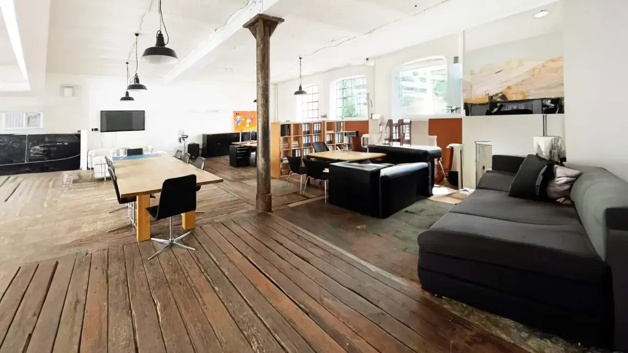 Geräumiges Loft mit Holzboden, großen Fenstern, Arbeitsbereich und gemütlicher Sitzecke. Eine perfekte loft definition.