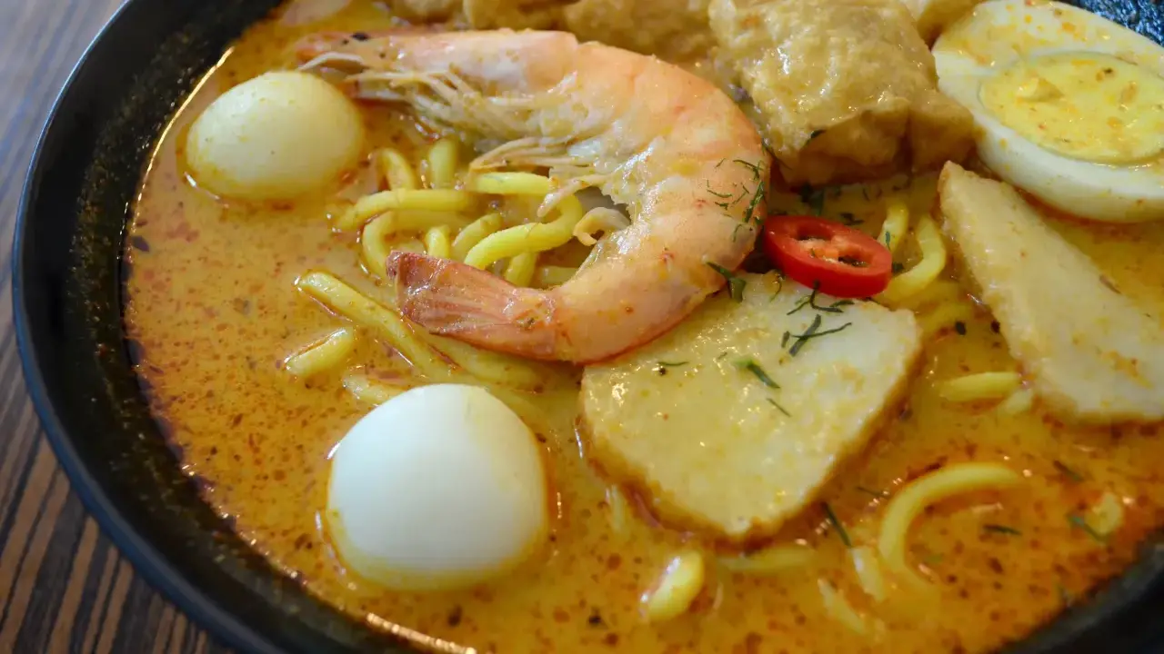 Eine Schüssel Laksa, ein beliebtes Singapur-Essen, mit Garnelen, Ei, Tofu und Nudeln in cremiger Kokosbrühe.