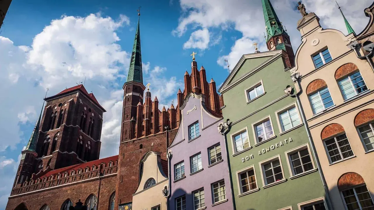 Kolorowe kamienice w Gdańsku pod błękitnym niebem z chmurami, w tle kościół.