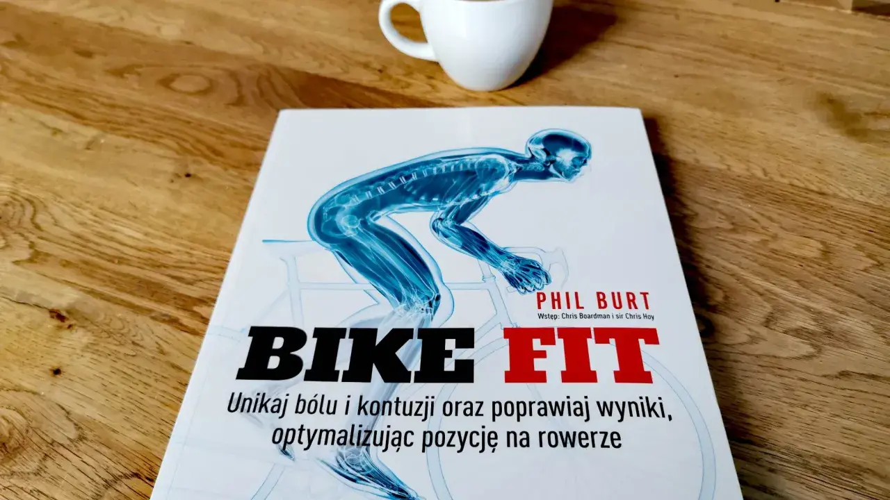 Książka "Bike Fit" z anatomicznym schematem rowerzysty i filiżanką kawy na drewnianym blacie.