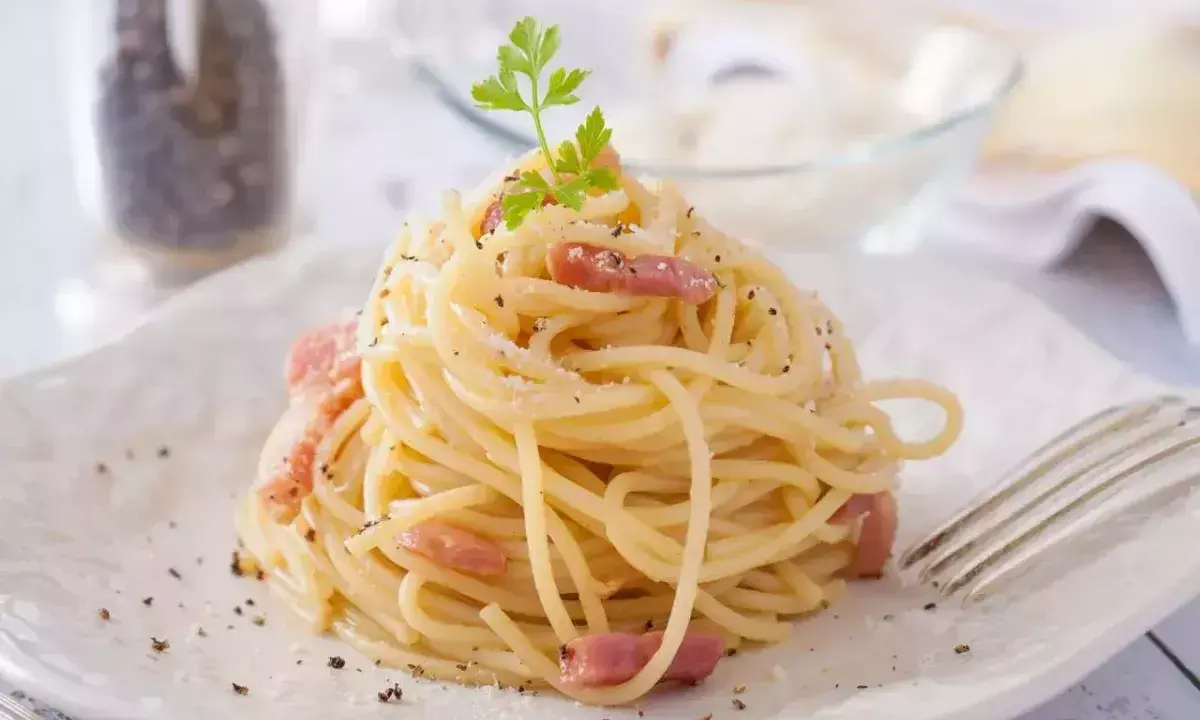 Un plat de tagliatelles carbonara crémeuses, garni de lardons et de persil frais, prêt à être dégusté.