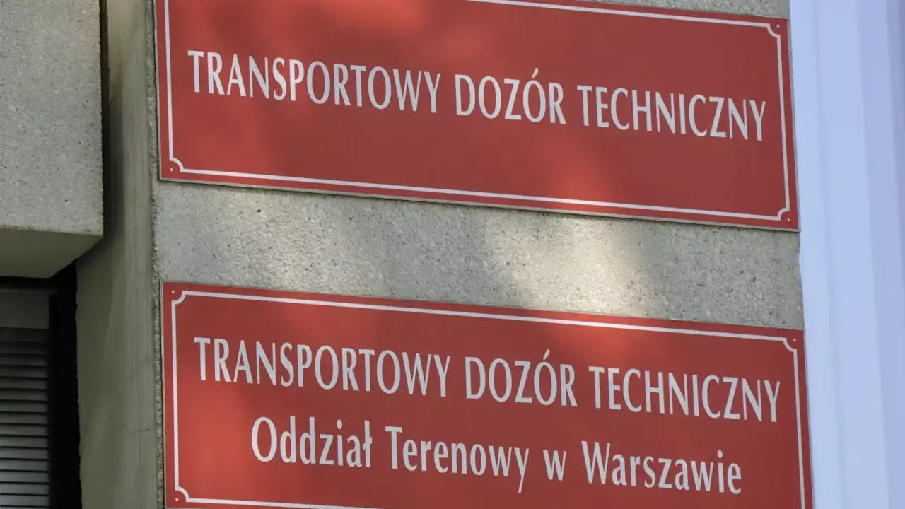Dwa czerwone szyldy z białym napisem "TRANSPORTOWY DOZÓR TECHNICZNY". Dolny szyld zawiera dodatkowo "Oddział Terenowy w Warszawie". Miejsce, gdzie można uzyskać homologację.