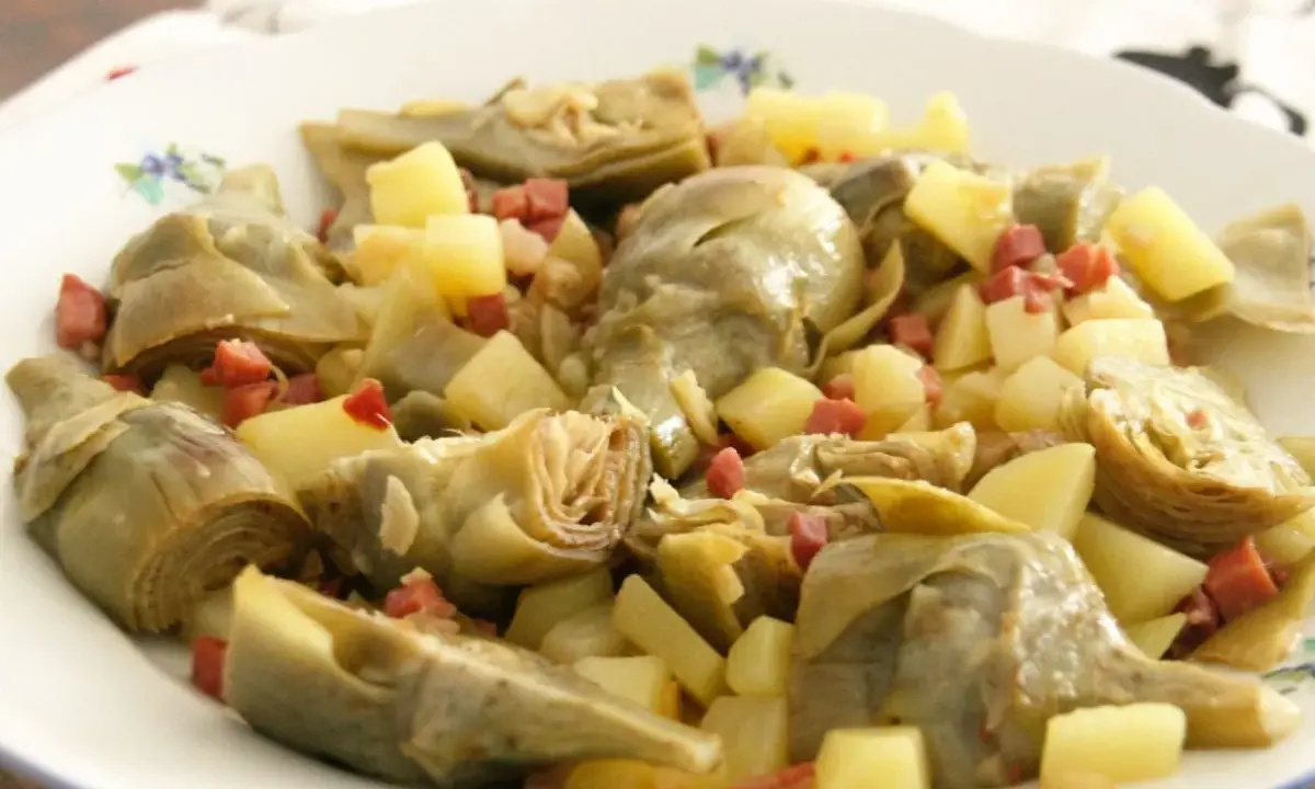 Plato de alcachofas tiernas y patatas cortadas en cubos, salpicado con trocitos de jamón. Un manjar casero.