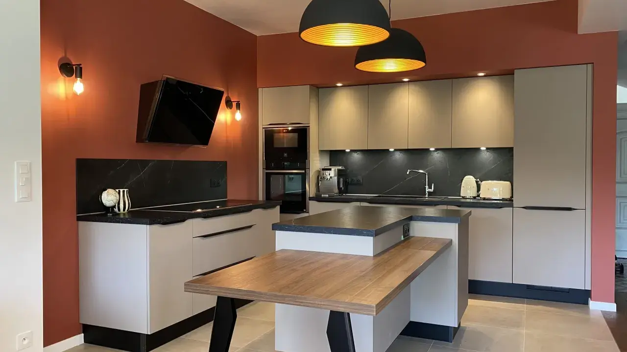 Cuisine moderne aux murs terracotta, avec îlot central en bois et mobilier gris clair. Éclairage chaleureux.