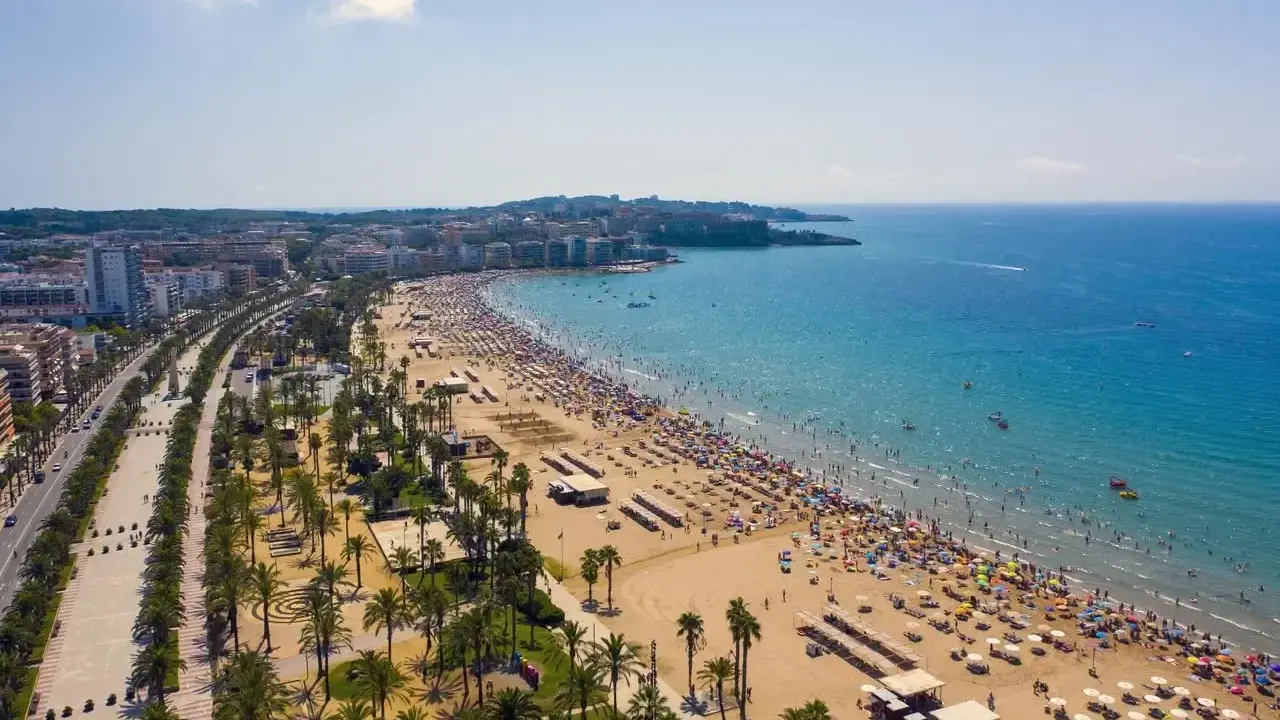 Tłum ludzi cieszy się słońcem na plaży, a w tle widać miasto. To idealne miejsce na wakacje, pełne atrakcji Costa Dorada.