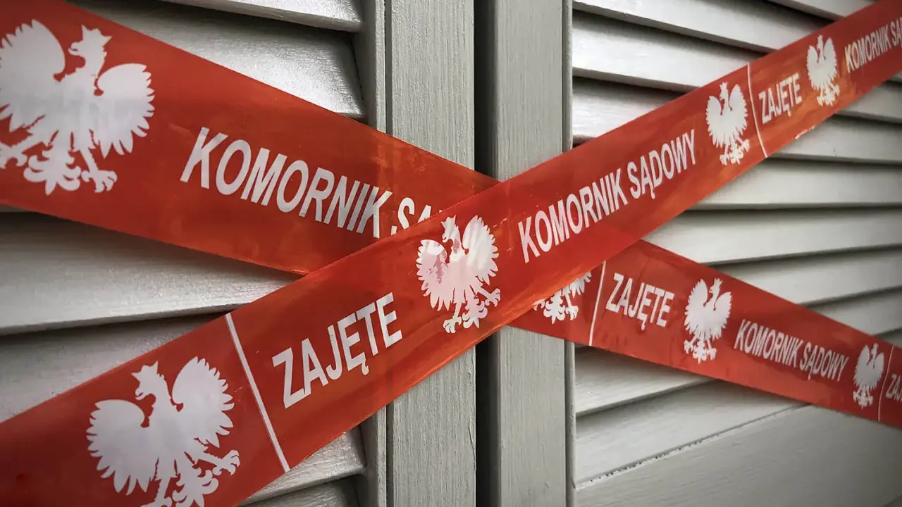 Czerwona taśma z napisem "KOMORNIK SĄDOWY" i godłem Polski krzyżuje się na szarej powierzchni. Jak pozbyć się komornika z konta?