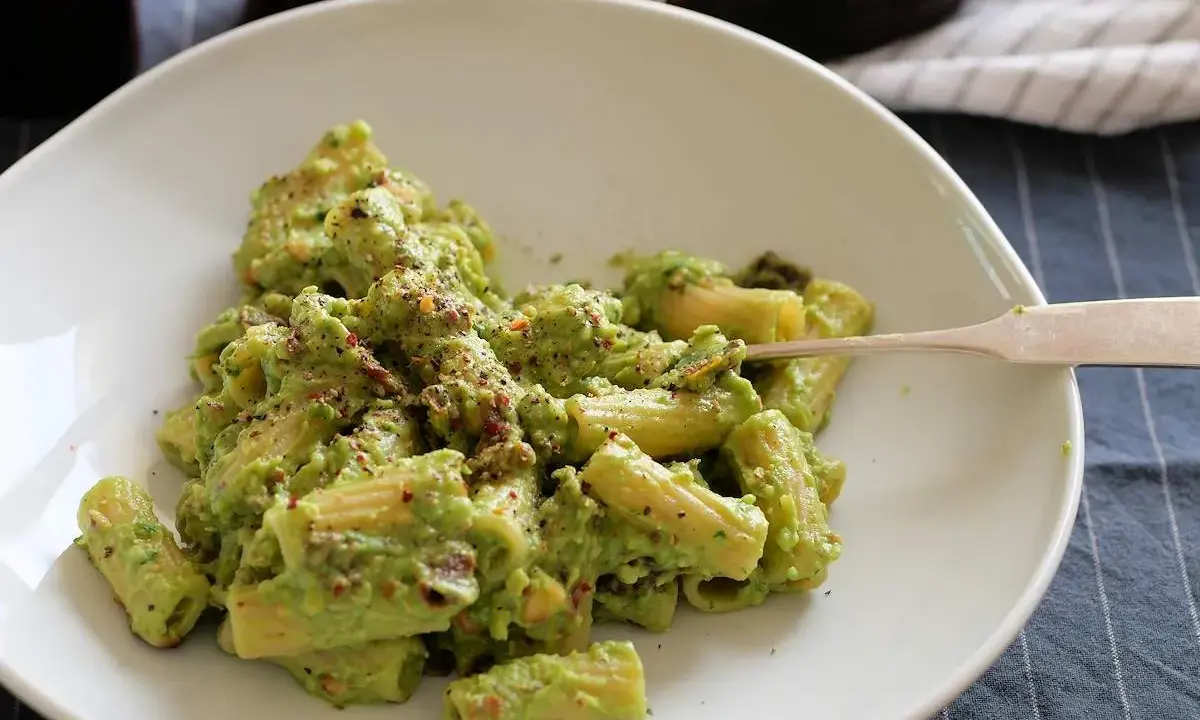 Cremige Avocado-Pasta mit Kräutern und Gewürzen auf einem weißen Teller, bereit zum Genießen.
