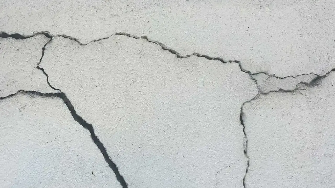 Pęknięcia na jasnej powierzchni betonu, świadczące o procesie karbonatyzacji.