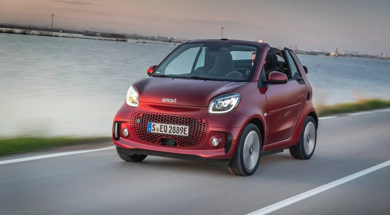 El Smart EQ Fortwo, cual es el coche más pequeño del mercado, se desplaza ágilmente por una carretera costera al atardecer.