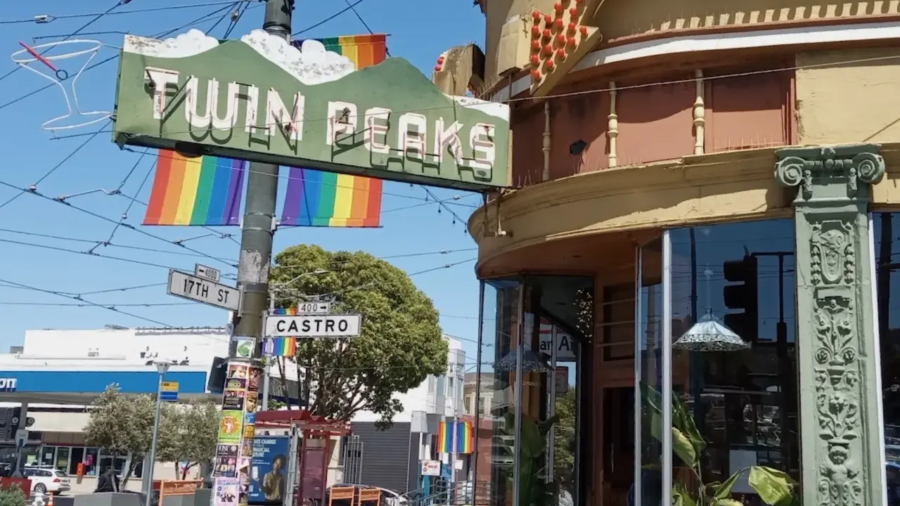 The iconic Twin Peaks sign hangs above Castro Street, a vibrant symbol of the gay area of San Francisco, adorned with rainbow flags.