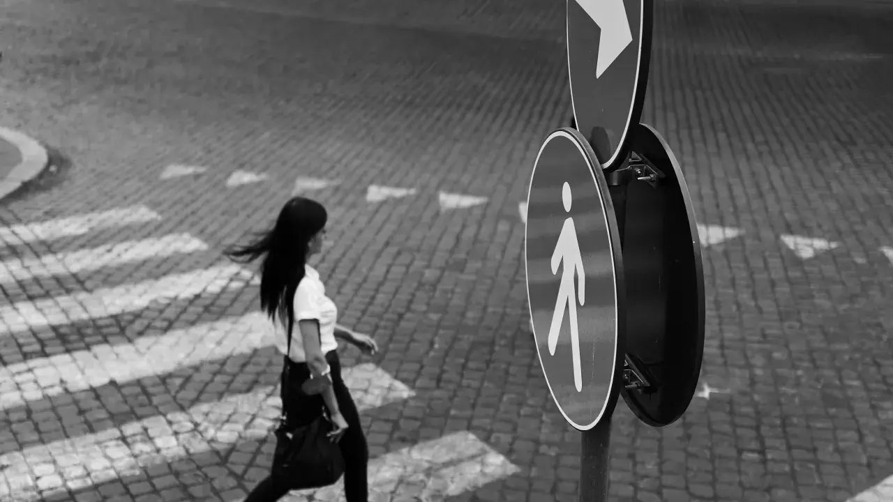Donna attraversa la strada, un momento catturato con la street photography tecnica. Segnali stradali indicano la direzione.