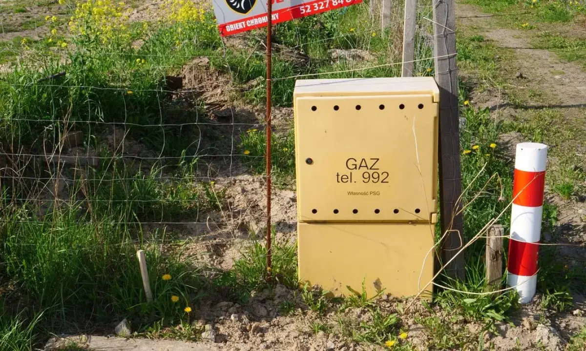 Żółta skrzynka gazowa z napisem "GAZ tel. 992" stoi obok ogrodzenia. Czy skrzynka gazowa musi być żółta?
