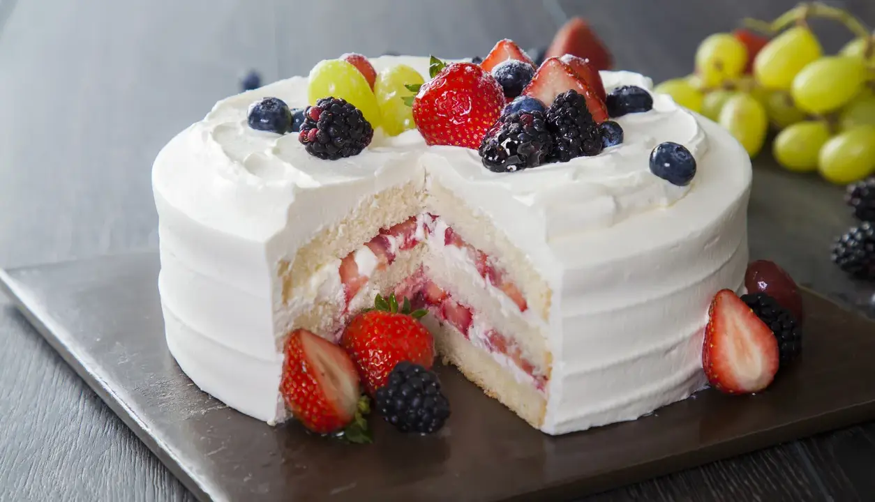 Pyszny tort z bitą śmietaną i mascarpone, przełożony truskawkami i owocami leśnymi. Udekorowany świeżymi owocami.