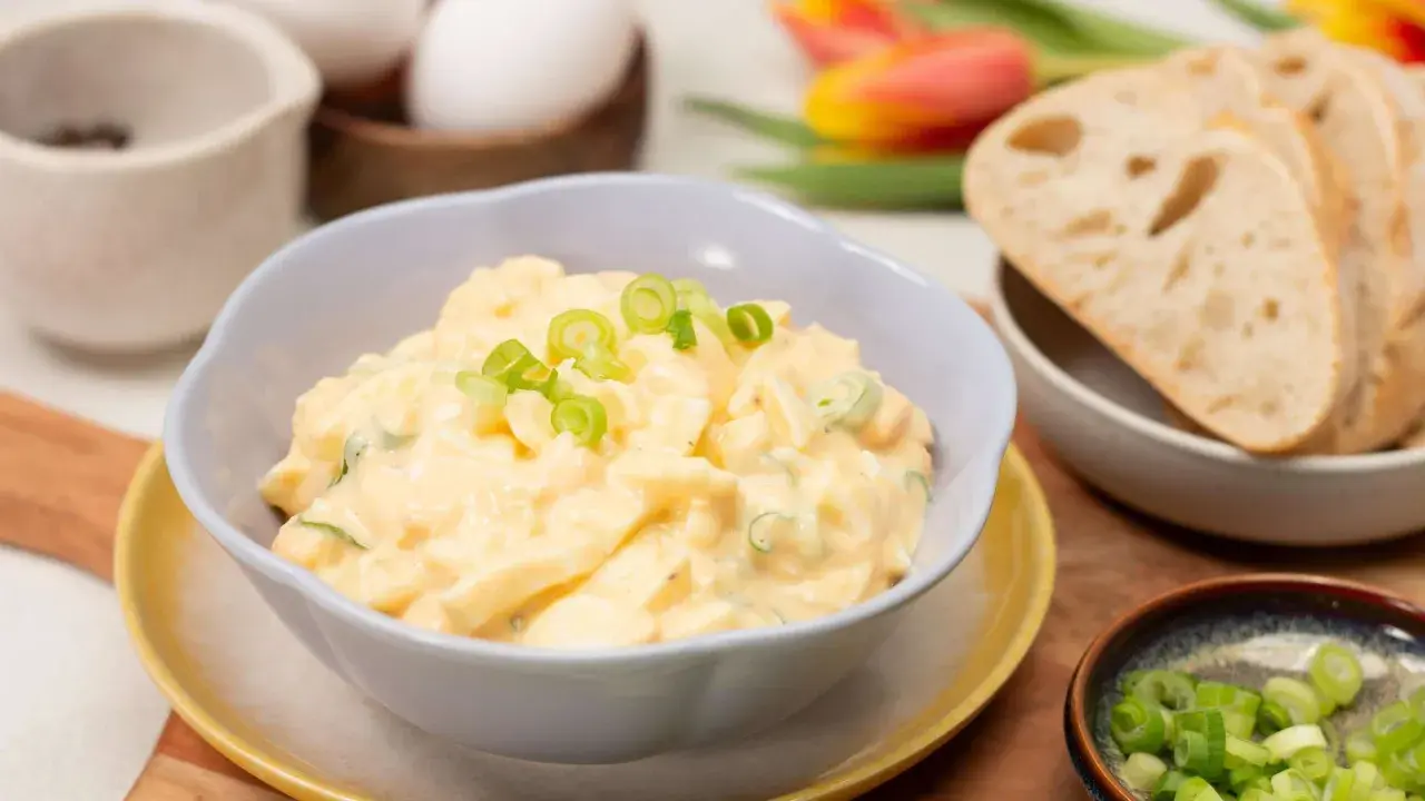 Cremiger Eiersalat mit Joghurt und Gurke, garniert mit Frühlingszwiebeln, serviert mit Brot.