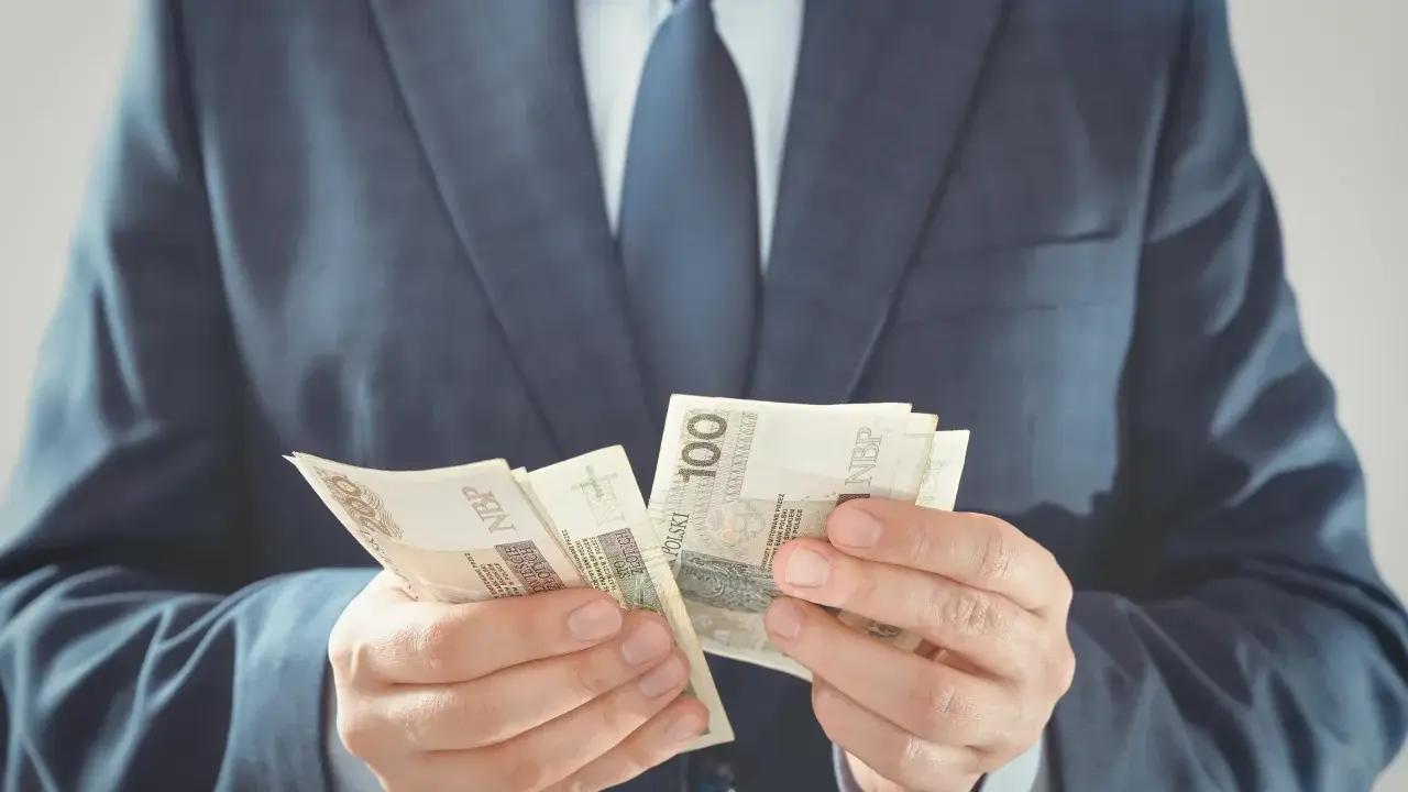 Mężczyzna w garniturze liczy banknoty 100 zł. To jego zabezpieczenie finansowe na przyszłość.
