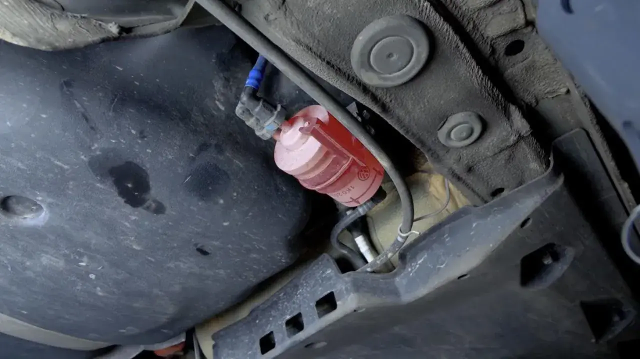 El filtro de combustible, de color rojo y transparente, está ubicado debajo del coche, cerca del tanque.