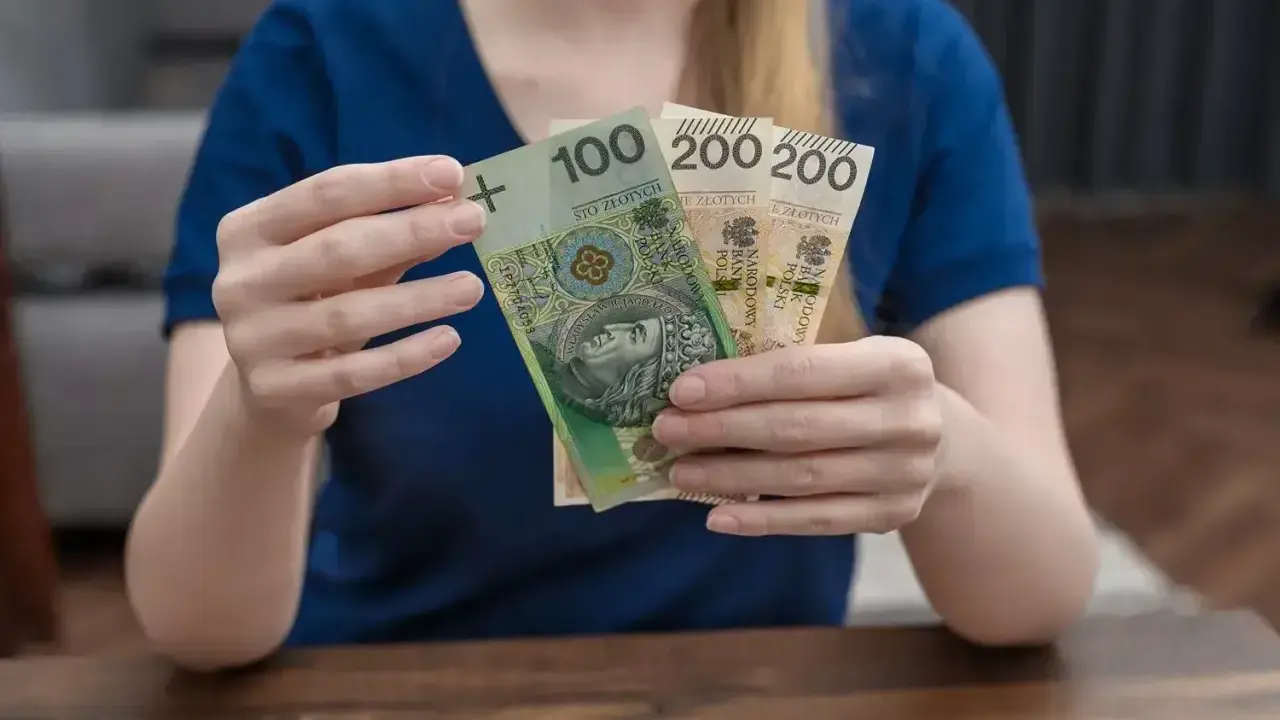 Kobieta trzyma polskie banknoty 100 i 200 zł. Zastanawia się, urlop macierzyński ile płatny.