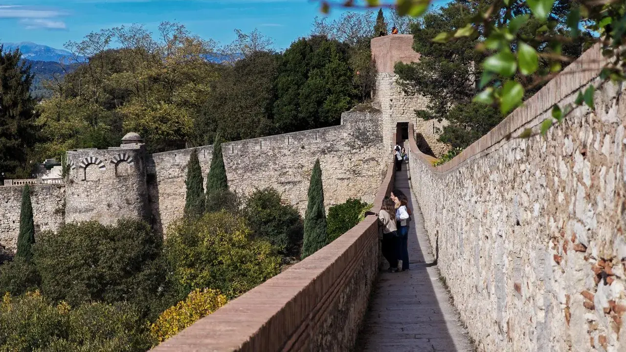 Spaziergang auf der Stadtmauer von Girona, Spanien. Zwei Frauen genießen die Aussicht auf die historische Festung und die grüne Landschaft.