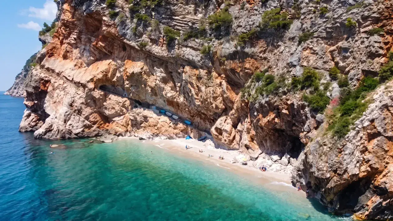 Versteckter geheimtipp kroatien strand: Eine kleine Bucht mit türkisfarbenem Wasser, umgeben von steilen Felsen. Einige Boote liegen am Ufer, wenige Menschen genießen die Ruhe.