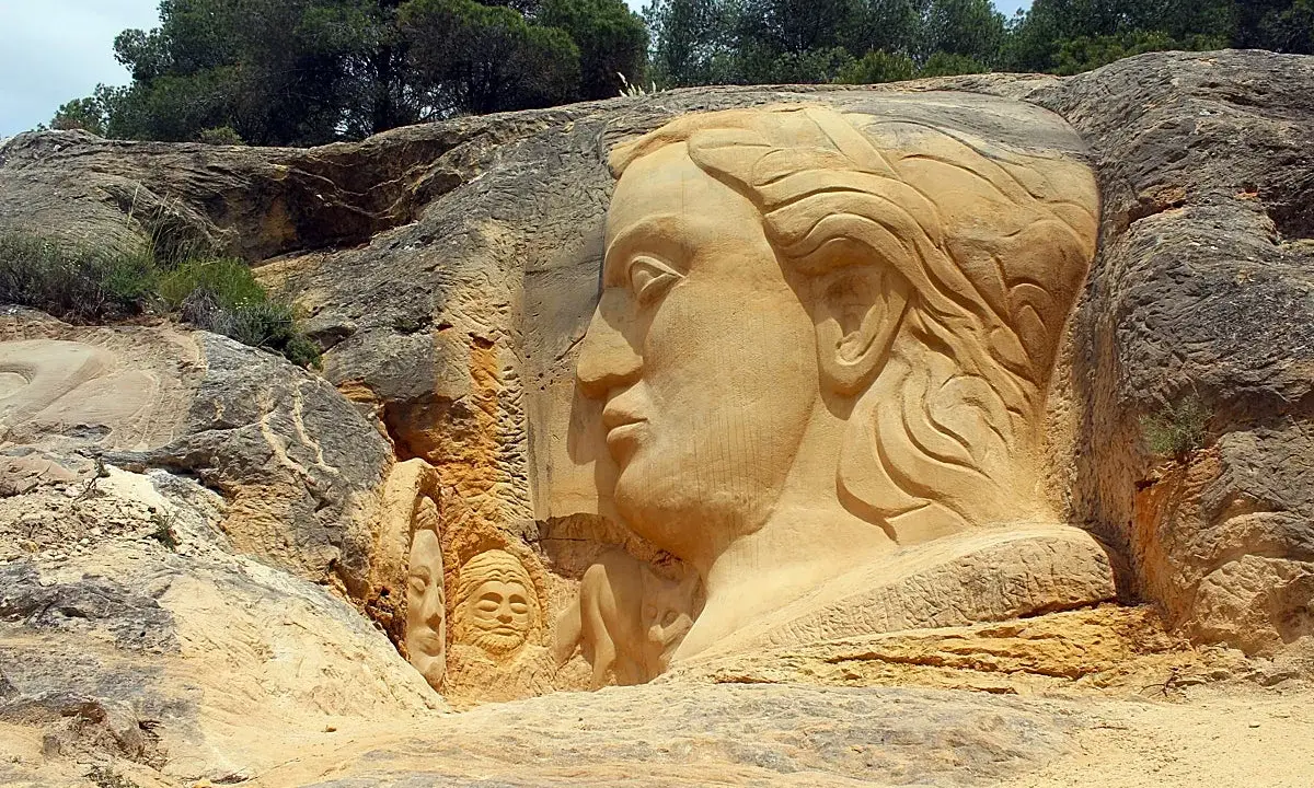 En la ruta de las esculturas, rostros emergen de la roca. Una gran cabeza femenina domina la escena, flanqueada por figuras más pequeñas.