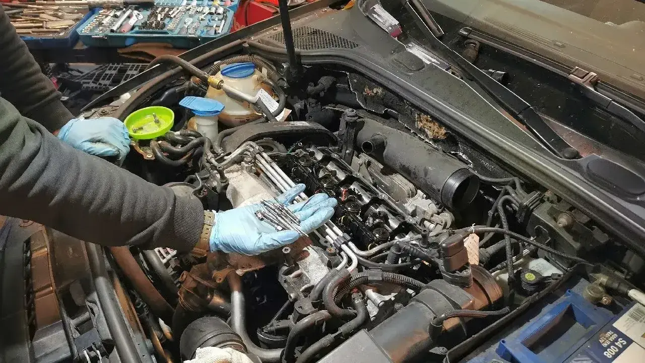 Mechanik w niebieskich rękawiczkach trzyma nowe świece żarowe, przygotowując się do ich wymiany w silniku samochodu.