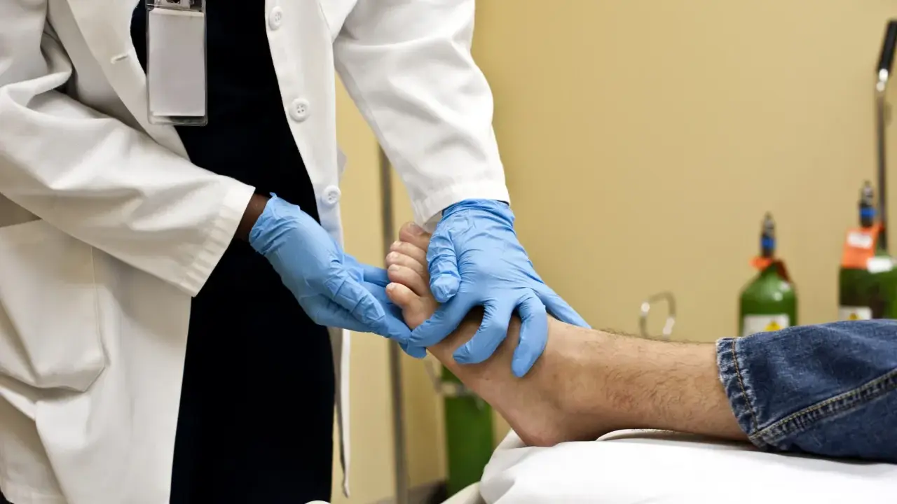 Un professionnel de santé examine un pied, possiblement pour une plaie diabétique, avec des gants bleus. L'application de bétadine est une étape courante pour le soin des plaies.