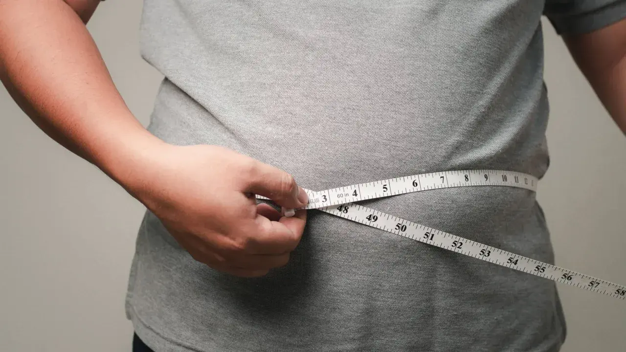 Eine Hand misst mit einem Maßband die Taille. Viele fragen sich, wo nimmt man zuerst ab – oft ist es der Bauch.
