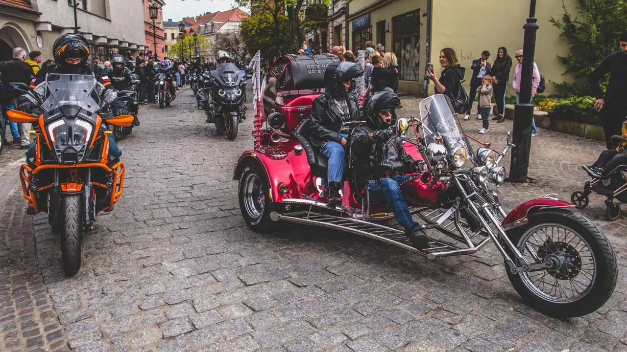 Parada motocykli i trójkołowców na brukowanej ulicy. W tle widzimy ludzi i budynki. To może być początek podróży szwecja motocyklem.
