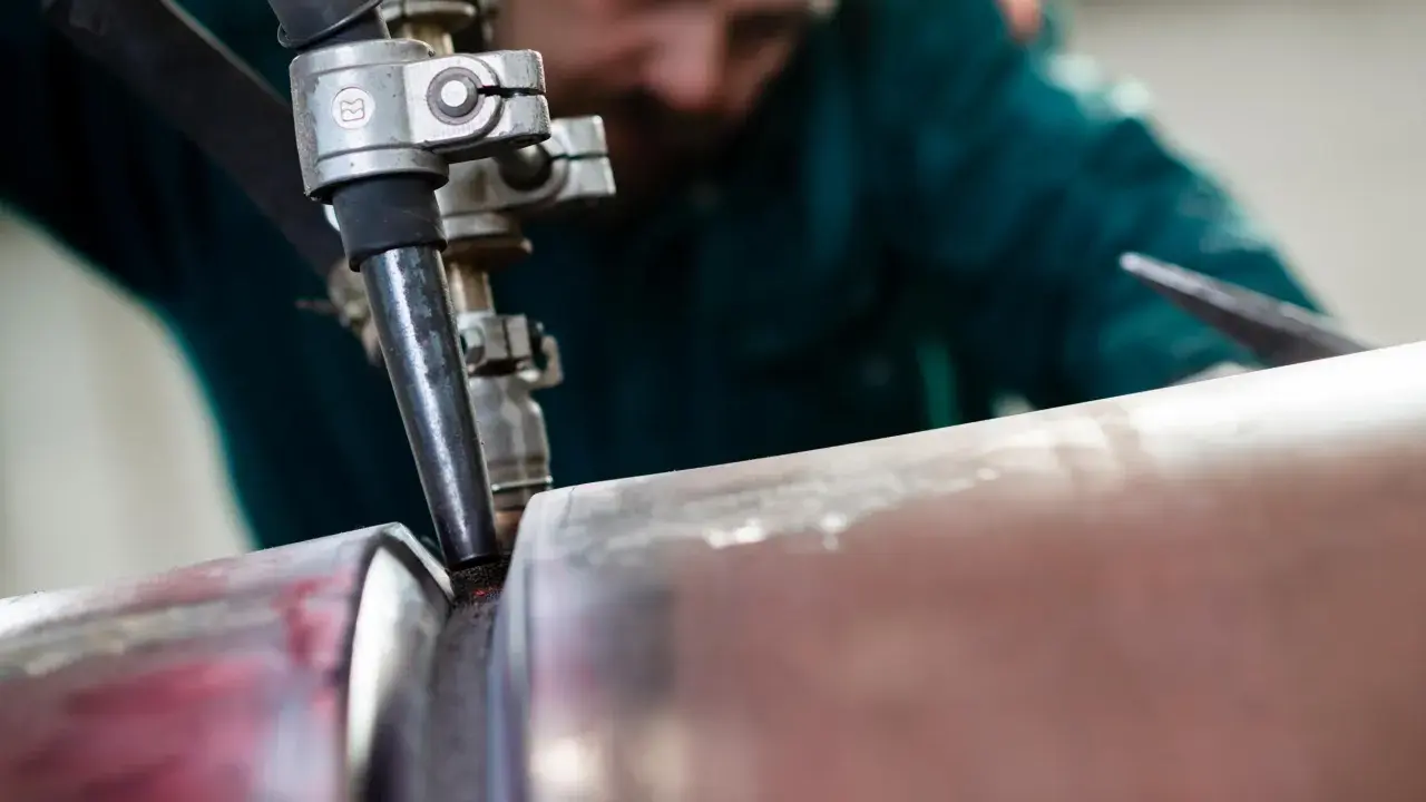 Saldatore esperto esegue saldatura ad arco sommerso su un tubo metallico, creando un giunto robusto.