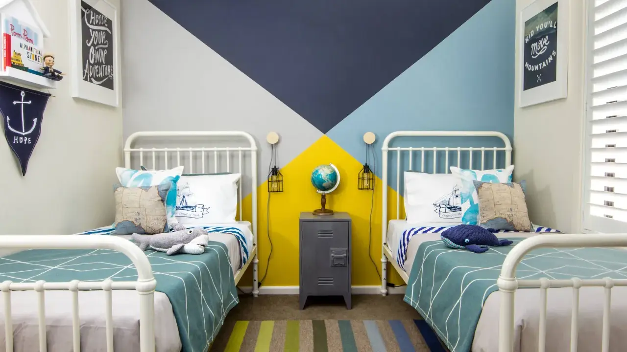 Habitaciones juveniles con camas blancas y pared geométrica en azul, gris y amarillo. Alfombra de rayas y decoración náutica.