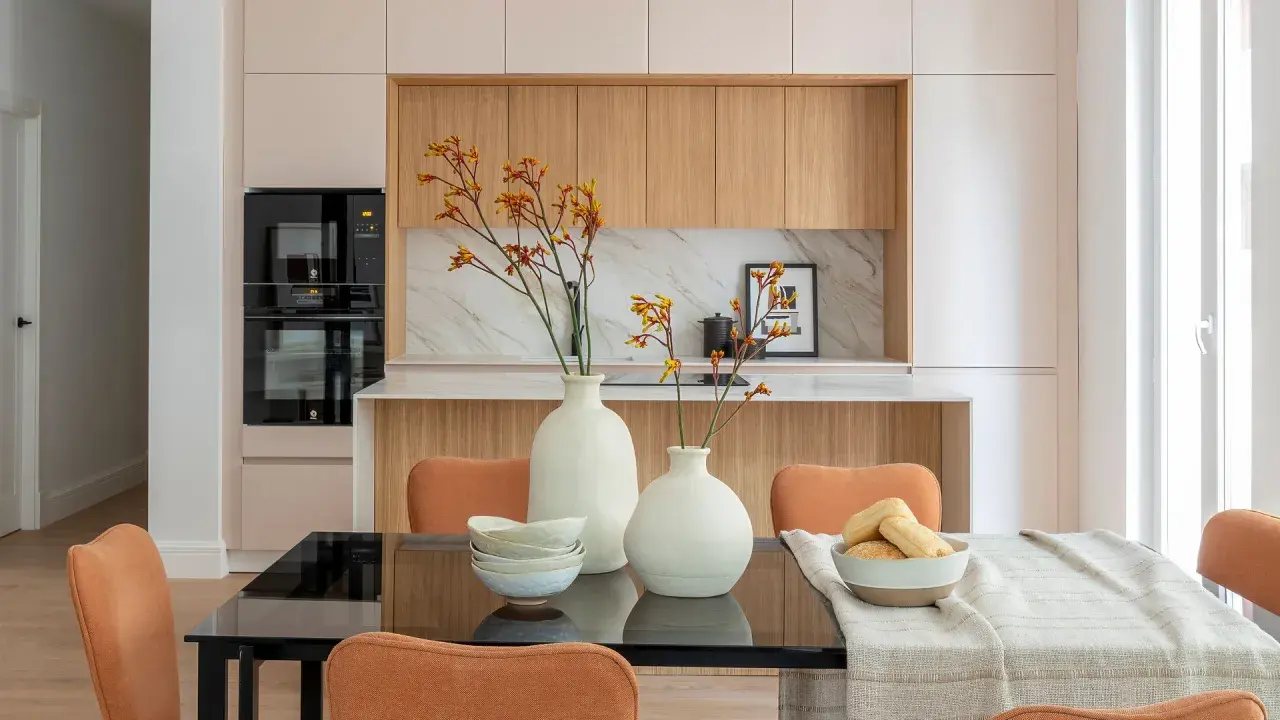Dos jarrones blancos con flores anaranjadas y amarillas, cuencos apilados y un bol con panecillos son elementos decorativos que poner encima de una mesa de comedor.