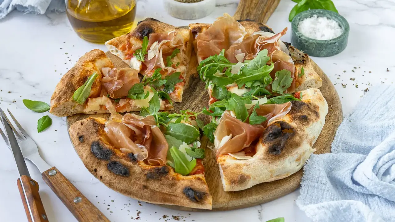 Pizza mit Prosciutto, Rucola und frisch gehobeltem Parmesan. Ein Genuss für alle Sinne!
