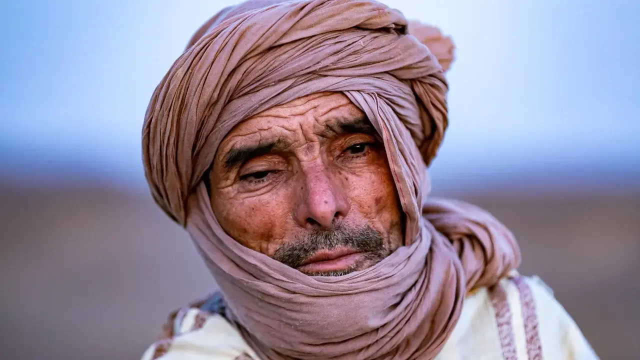 Porträt eines alten Berber Hirtennomaden mit einem Turban und traditioneller Kleidung, dessen Gesicht von der Sonne gezeichnet ist.