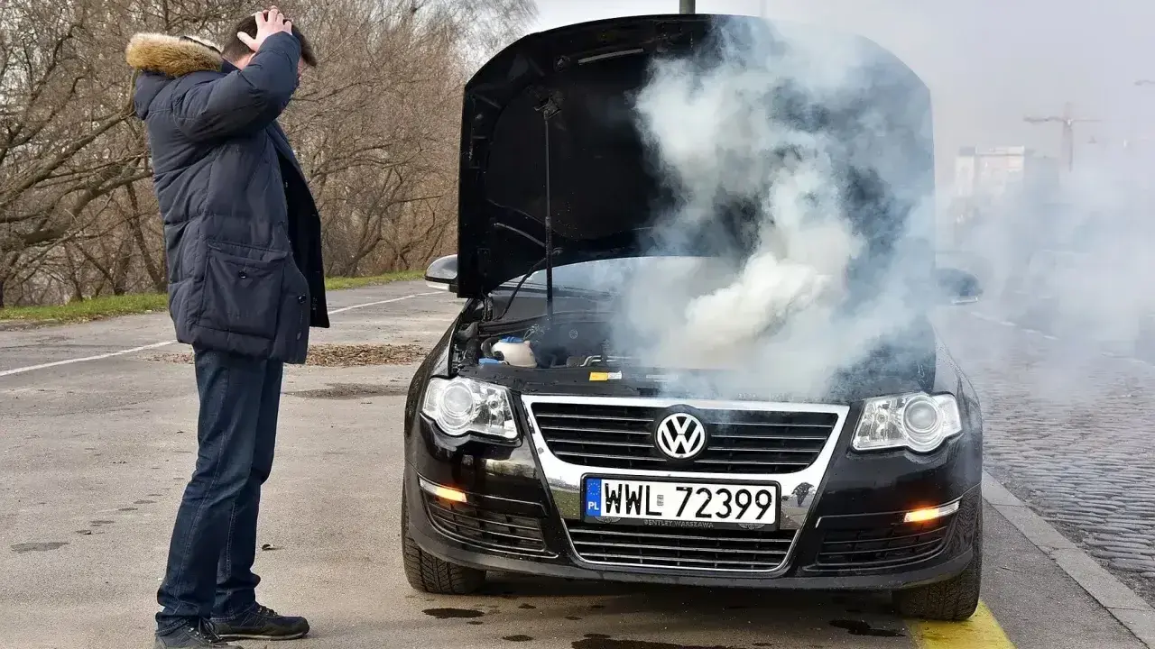 Mężczyzna zrezygnowany patrzy na dymiący, lekko przytarty silnik czarnego Volkswagena.